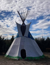 A single Tipi with trees and blue sky skies and white fluffy clouds in background